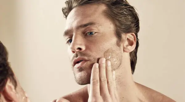 Un homme applique un soin sur sa barbe qui pique, sa main caresse sa joue.