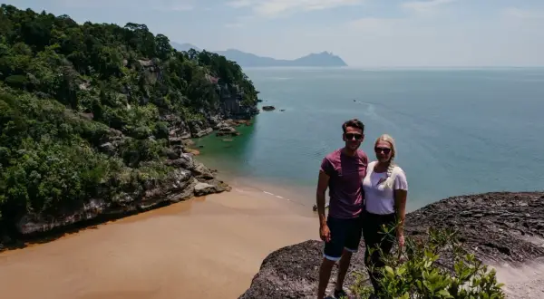 Ein Paar genießt die Aussicht auf eine tropische Bucht mit Sandstrand und Dschungel. Tolle Malaysia Urlaub Erfahrungen!