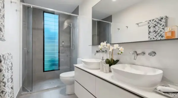 Elegantes baños modernos con ducha, lavabos dobles y ventana azul.