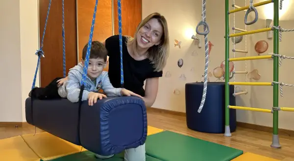 Kobieta i chłopiec w sali terapeutycznej z huśtawką i drabinką.