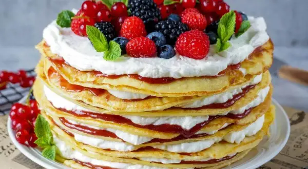Eine hohe Pfannkuchen Torte mit Sahne und roter Marmelade, gekrönt mit frischen Beeren und Minze.