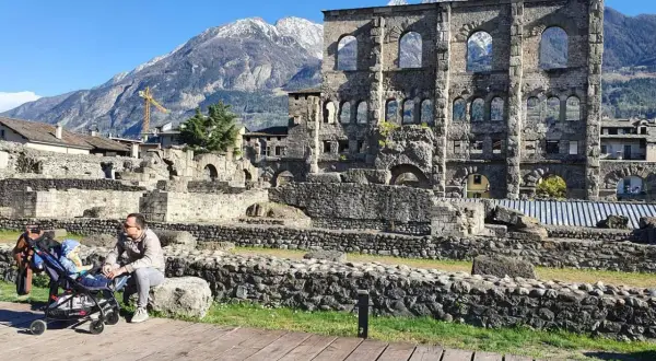 Un uomo con un passeggino ammira le rovine romane, uno dei **paesi più belli della Valle d'Aosta**, con montagne innevate sullo sfondo.