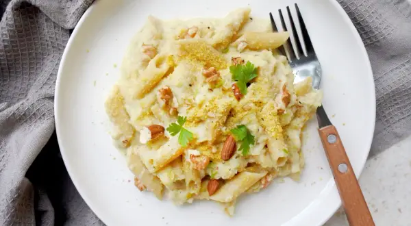 Penne z kremowym sosem z kalafiora, orzechami i natką pietruszki. Pyszny makaron z kalafiorem na białym talerzu.