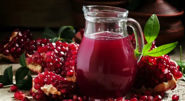 Sok z granatu w ciąży to zdrowy wybór. Na zdjęciu dzbanek z rubinowym sokiem i świeże granaty.