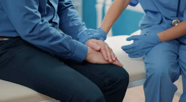 Pielęgniarka w niebieskich rękawiczkach pociesza pacjenta po operacji prostaty, który zmaga się z nietrzymaniem moczu.