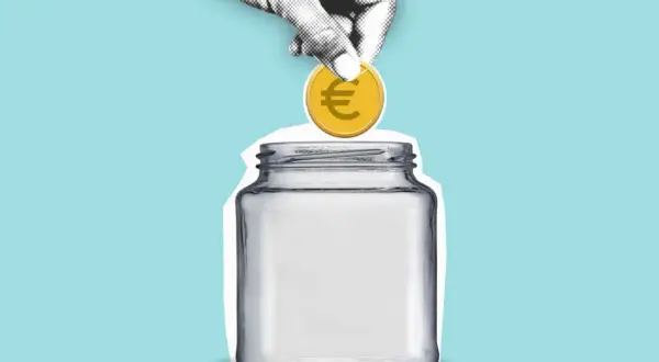 Eine Hand wirft eine Münze mit Euro-Symbol in ein leeres Glas. Sparen für den hauskauf steuer absetzen.