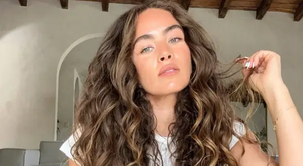 Mujer con un espectacular pelo rizado castaño, con reflejos dorados, acariciando un mechón.