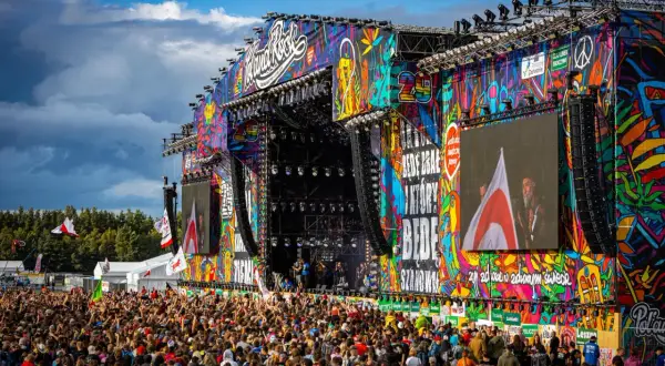 Kolorowa scena festiwalu polandrock 2026 z tłumem fanów. Na ekranach widać artystów, a nad nimi tęczowe grafiki.