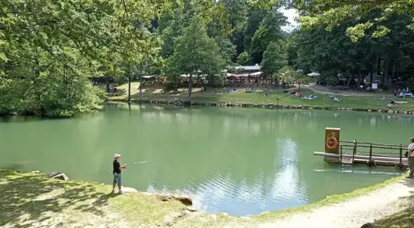 Un ragazzo pesca sul lago Pontini, mentre altre persone si rilassano sull'erba.
