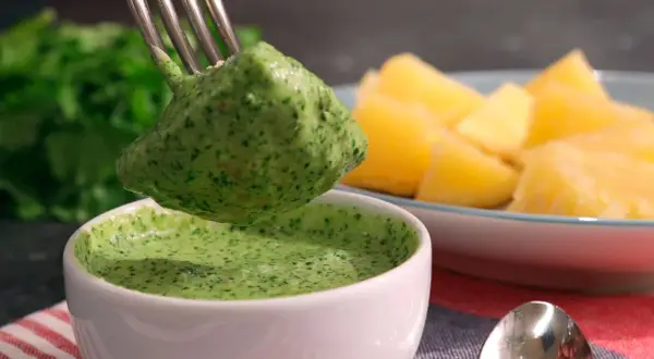 Un tenedor recoge una porción de mojo verde canario, una salsa vibrante, junto a papas arrugadas.