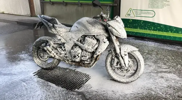 Motocykl pokryty pianą na myjni bezdotykowej. Instrukcja obok podpowiada, jak myć motocykl, by był lśniący.