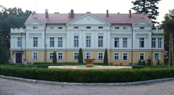 Pałac w Sasinie, z fontanną i zadbanym ogrodem, otoczony drzewami.