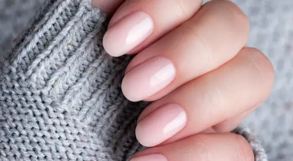 Delikatne, różowe paznokcie na tle szarego swetra. Dowiedz się, jak stosować bazę kauczukową Niuqi dla idealnego manicure.