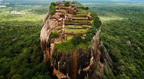 Imponerande ruiner på toppen av en klippa, som en fästning. En vy som påminner om Adams Peak, omgiven av frodig djungel.