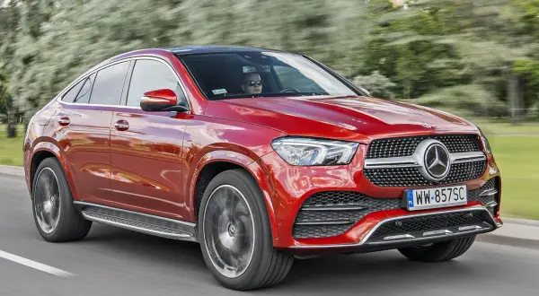 Czerwony Mercedes-Benz GLE Coupe, model gle amg, pędzi po drodze, za kierownicą siedzi kierowca w okularach.