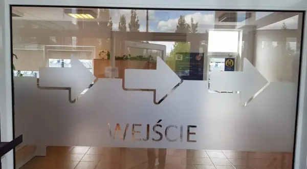 Szklane drzwi z matowymi strzałkami i napisem "WEJŚCIE".