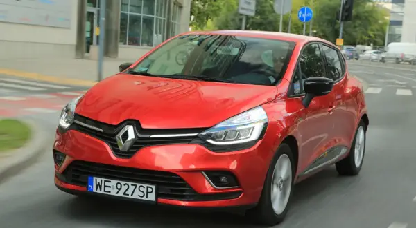 Czerwony Renault Clio 3 1.2 benzyna w ruchu miejskim. Kierowca w okularach przeciwsłonecznych.