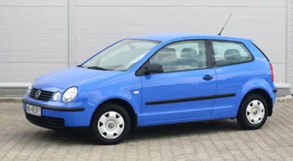 Niebieski Volkswagen Polo 1.2 benzyna, widok z boku. Auto stoi na kostce brukowej przed szarym budynkiem.