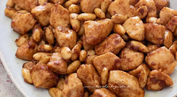 Un invitante pollo alle mandorle, con bocconcini dorati e mandorle tostate, servito su un piatto bianco.