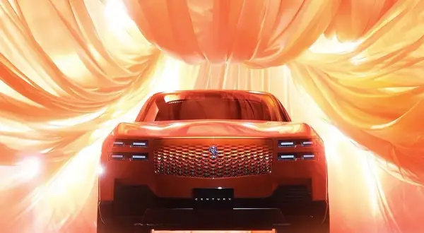 Nowy Toyota Century w pomarańczowym odcieniu, otoczony falującymi, złotymi tkaninami, prezentuje swoją luksusową kratę i reflektory.