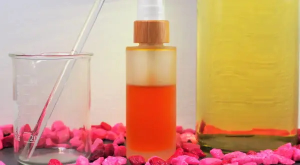 Zutaten für anti aging creme selber machen: ein Becherglas mit Pipette, eine Sprühflasche mit orangefarbener Flüssigkeit und ein großes Glas mit gelbem Öl.