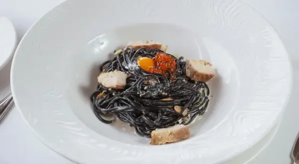 Pasta negra con trozos de pescado, huevas de salmón y yema de huevo. La tinta de calamar, ingrediente principal, aporta un sabor único y propiedades beneficiosas.