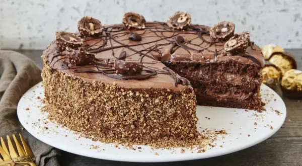 Schokoladentorte mit Ferrero Rocher verziert, die Seiten sind mit gehackten Nüssen bedeckt. Ein Stück fehlt, was Lust auf mehr macht.