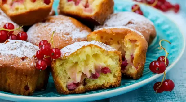Puszyste muffinki z czerwoną porzeczką, posypane cukrem pudrem, kuszą swoim wyglądem. Idealne na letnie popołudnie.