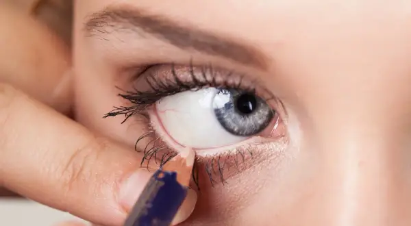 Una mano applica una matita bianca per illuminare la rima interna dell'occhio, un trucco per ingrandire lo sguardo.