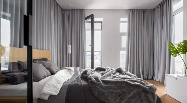 Nowoczesne rodzaje zasłon w sypialni, tworzące przytulną atmosferę. Szare tkaniny okrywają okna i drzwi balkonowe, dodając elegancji.