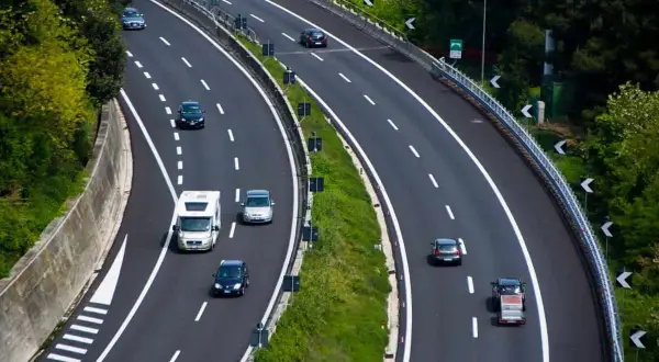 Autostrada z samochodami i kamperem, otoczona zielenią.