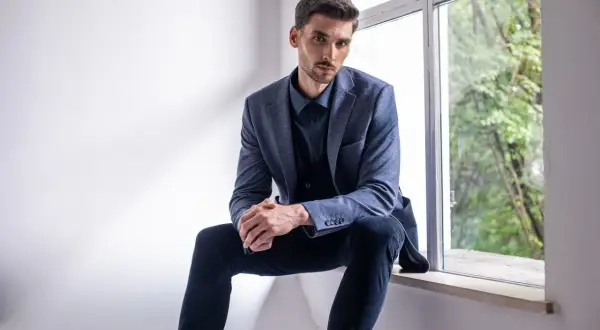 Elegancki mężczyzna w granatowej koszuli i marynarce, zastanawia się, jakie spodnie do niebieskiej koszuli będą najlepszym wyborem.