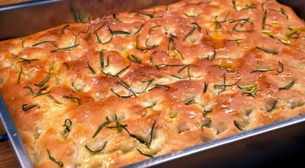 En gyllene focaccia barese med rosmarin och flingsalt i en form. Doftar ljuvligt!