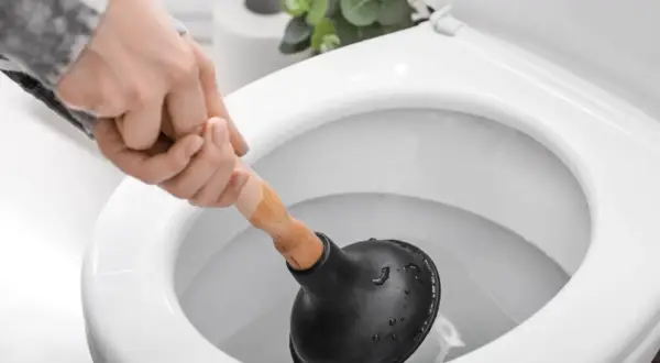 Hand mit Saugglocke versucht, eine verstopfte Toilette zu befreien.