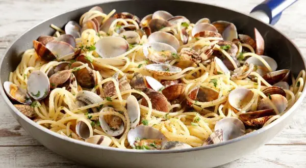 Un piatto invitante di spaghetti con le vongole, condito con prezzemolo fresco, servito in una padella su un tavolo di legno.
