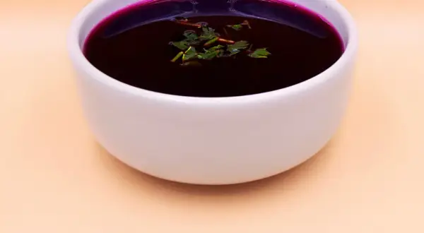 Aromatic barszcz czerwony domowy, głęboki kolor buraków, ozdobiony świeżymi ziołami, w białej miseczce.