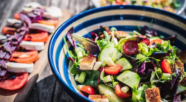 En matig sallad med allt om mat: färska grönsaker, krutonger och mozzarella på en träplanka.