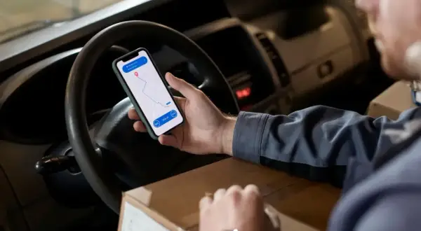 Kierowca sprawdza trasę na telefonie, trzymając paczkę. Aplikacja nawigacyjna pokazuje punkty odbioru i dostawy, ułatwiając pracę w **srs dpd**.