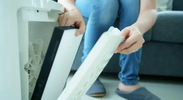 Osoba wyjmuje filtr z oczyszczacza powietrza. Czy filtr HEPA można myć wodą? Zależy od modelu, ten wygląda na jednorazowy.