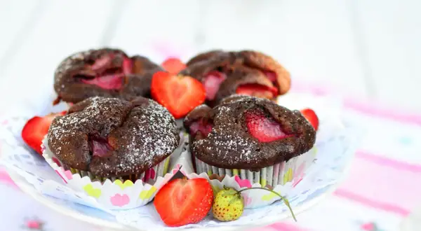 Pyszne muffiny czekoladowe z truskawkami, posypane cukrem pudrem, prezentują się apetycznie na talerzyku.