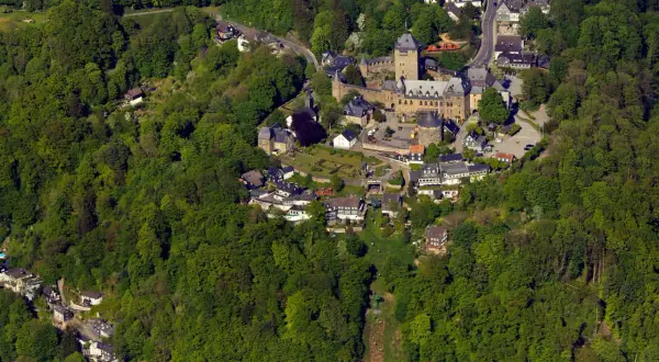 Luftaufnahme eines Schlosses, eingebettet in grüne Wälder. Die Burg ist ein beliebter Ort für Veranstaltungen und Ausflüge.