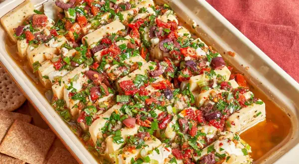 Un plat de fromage blanc coupé en tranches, garni d'olives, de tomates séchées et d'herbes. Une excellente idée repas pour l'apéritif.