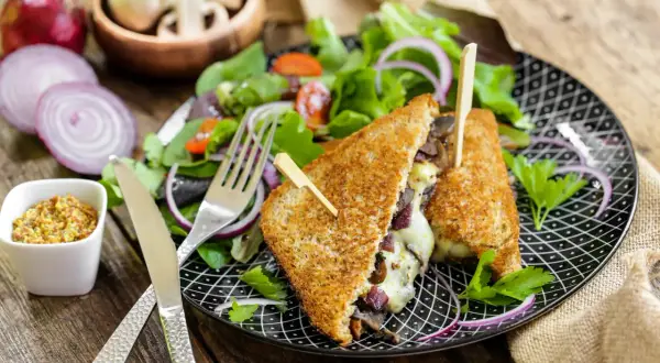 Un délicieux croque monsieur végétarien garni de champignons et de fromage fondant, servi avec une salade fraîche et de la moutarde à l'ancienne.
