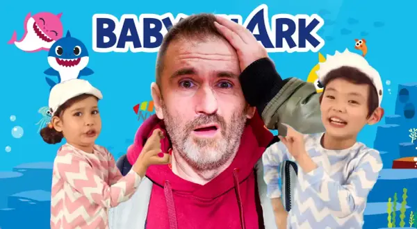 Zaskoczony mężczyzna otoczony przez dzieci i animowane rekiny, w tle napis "Baby Shark" – piosenka, która podbiła świat.