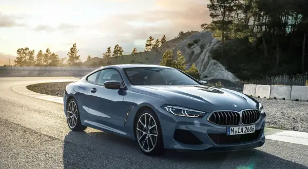 Szary BMW 840d na zakręcie toru wyścigowego, z drzewami i skalistym zboczem w tle.