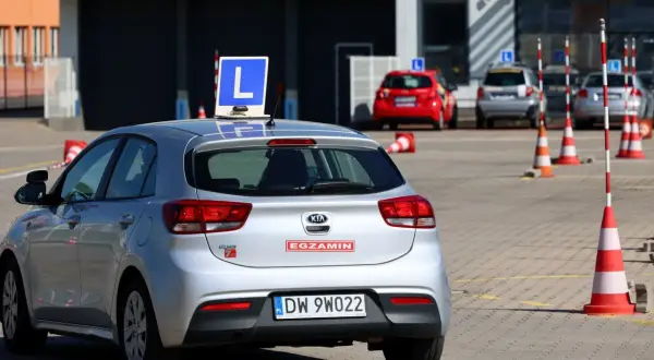 Srebrny samochód z literą "L" na dachu, gotowy do egzaminu. Dofinansowanie do prawa jazdy może pomóc w nauce jazdy na takim pojeździe.