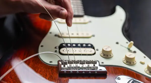 Dłoń naciąga nowe struny w gitarze elektrycznej, przygotowując ją do gry.