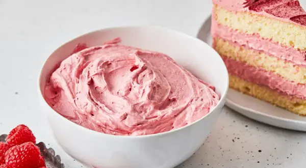 Schüssel mit cremiger Buttercreme mit Pudding und Himbeeren. Daneben ein Stück Kuchen mit derselben Füllung.