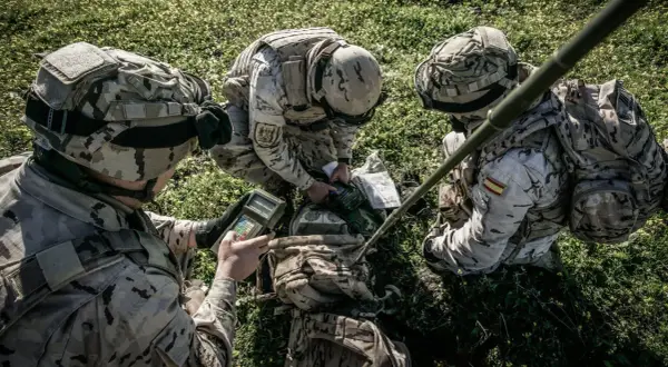 Soldados del ejército español con uniforme multicam revisan equipo en el campo.