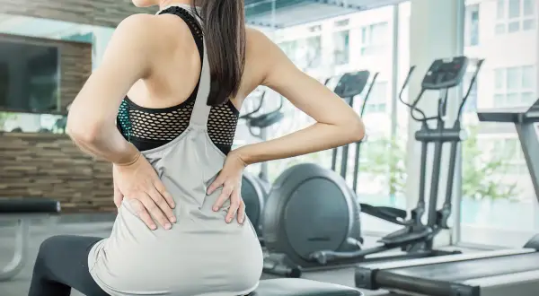 Donna in palestra con le mani sulla schiena, soffre di mal di schiena. Attenzione agli esercizi da evitare in palestra per il mal di schiena.